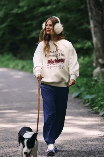 Woman walking a dog in an oversized sweatshirt and sweatpants.